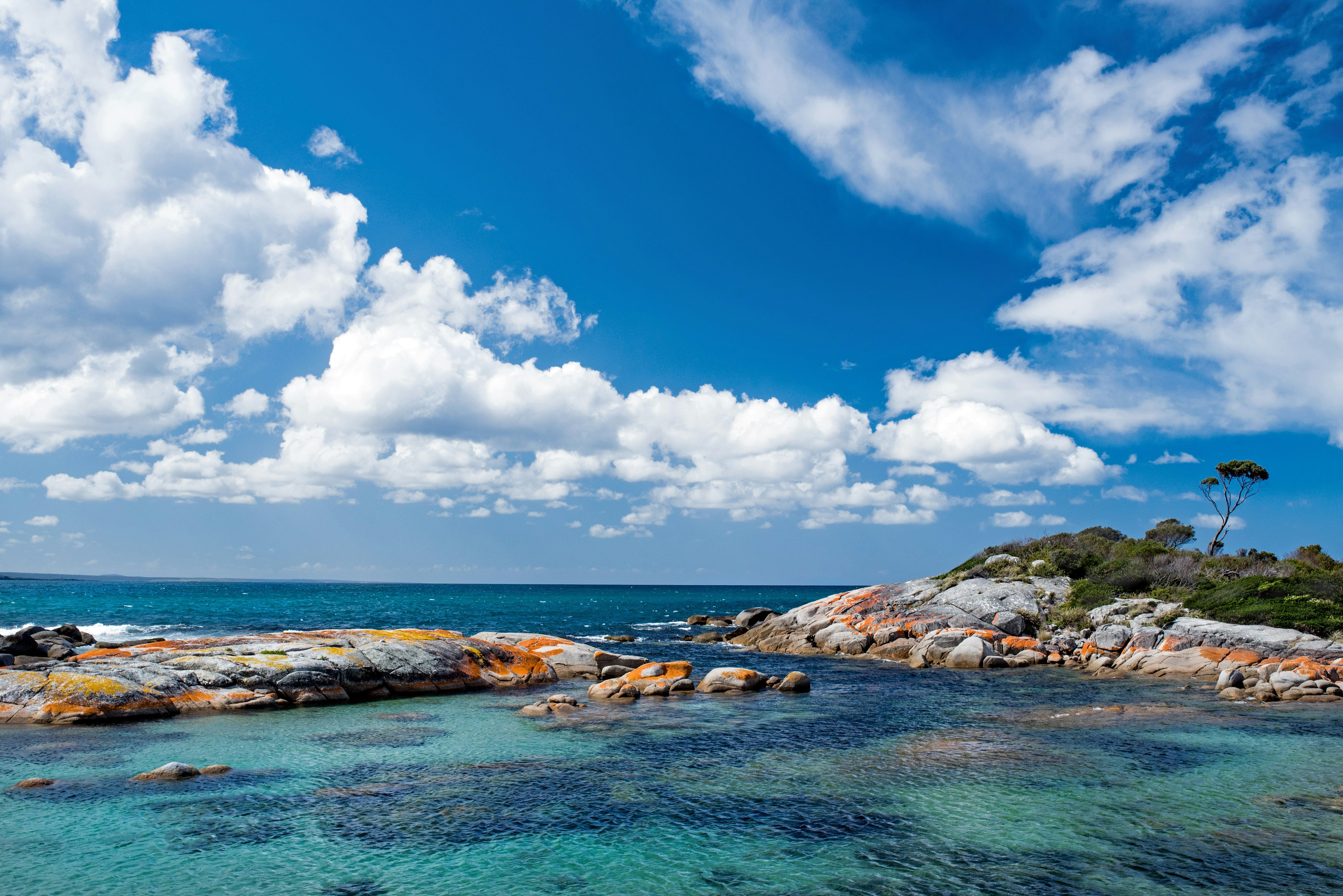 The Bay of Fires coastline in Tasmania, with orange lichen-covered granite boulders, white sand, and clear blue water.